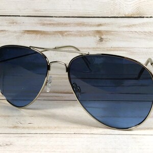 May include: Aviator sunglasses with a silver frame and blue lenses. The lenses have a gradient effect, transitioning from a darker blue at the top to a lighter shade at the bottom. The sunglasses are set against a light wood background.