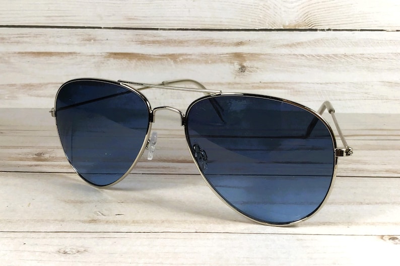 May include: Aviator sunglasses with a silver frame and blue lenses. The lenses have a gradient effect, transitioning from a darker blue at the top to a lighter shade at the bottom. The sunglasses are set against a light wood background.