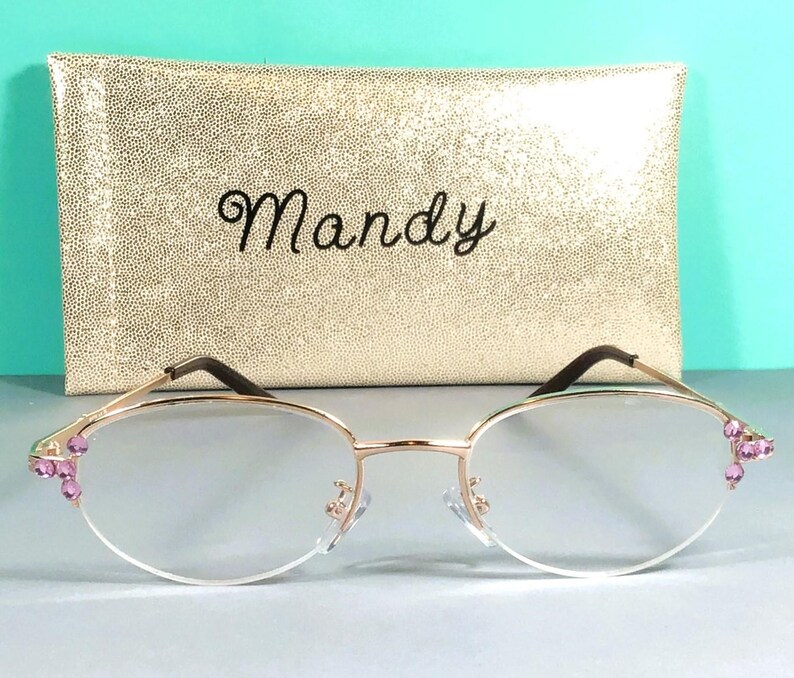 May include: Gold-rimmed spectacles with clear lenses and pink gemstone embellishments on the corners. The spectacles are presented with a gold, textured case inscribed with the name "Mandy".