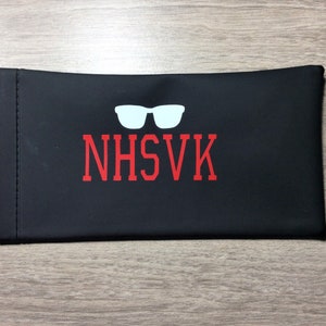 May include: Black eyeglass case with a white silhouette of sunglasses and the text "NHSVK" in red.