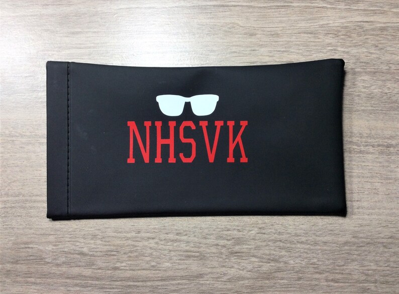 May include: Black eyeglass case with a white silhouette of sunglasses and the text "NHSVK" in red.
