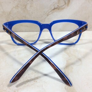 May include: Blue eyeglasses with a rectangular frame and brown and white patterned temples. The temples feature small, blue decorative accents. The glasses are designed for vision correction and fashion.