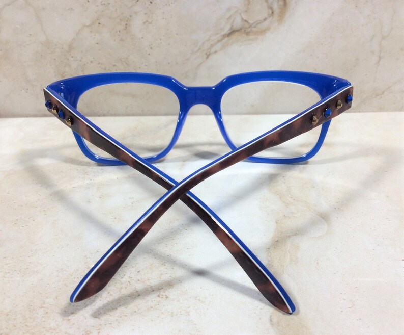 May include: Blue eyeglasses with a rectangular frame and brown and white patterned temples. The temples feature small, blue decorative accents. The glasses are designed for vision correction and fashion.