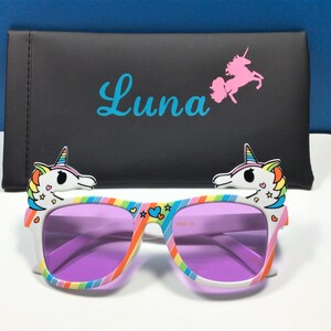 May include: Purple tinted sunglasses with a rainbow and white unicorn design. The sunglasses come with a black case that has the name "Luna" and a pink unicorn printed on it.
