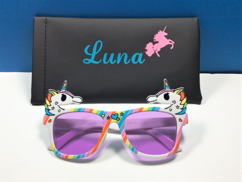 May include: Purple tinted sunglasses with a rainbow and white unicorn design. The sunglasses come with a black case that has the name "Luna" and a pink unicorn printed on it.