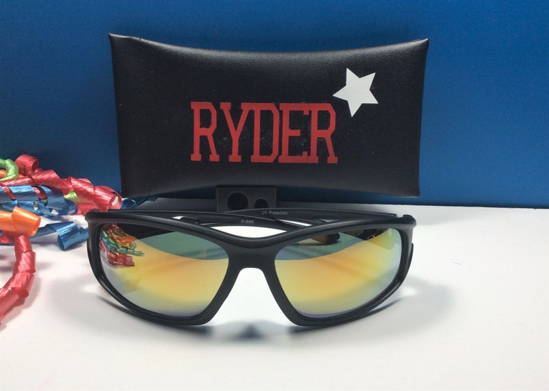 Puede incluir: Gafas de sol negras con lentes espejados y una funda negra con el nombre "RYDER" y una estrella blanca impresa.
