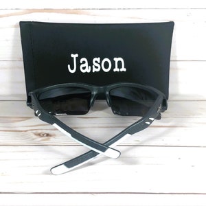 K&ouml;nnte beinhalten: Schwarze Sonnenbrille mit wei&szlig;en Akzenten und einem schwarzen Etui mit dem Namen "Jason" darauf.