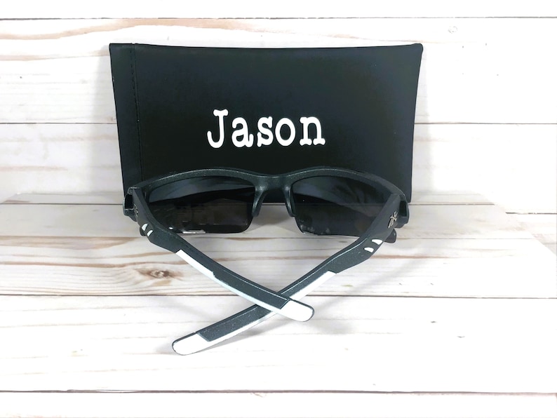 K&ouml;nnte beinhalten: Schwarze Sonnenbrille mit wei&szlig;en Akzenten und einem schwarzen Etui mit dem Namen "Jason" darauf.