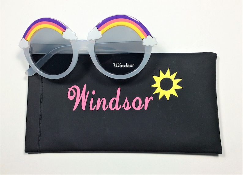 Puede incluir: Gafas de sol blancas con un dise&ntilde;o de arco&iacute;ris y nubes en el marco. Las gafas de sol vienen con una funda de transporte negra con un sol amarillo y la palabra "Windsor" impresa en rosa.