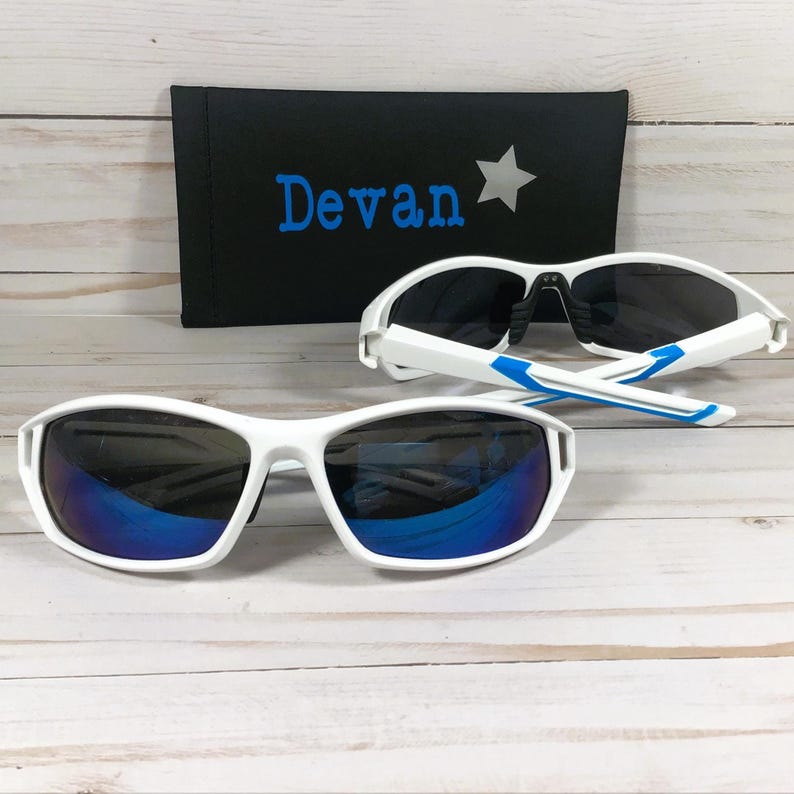 May include: White sports sunglasses with blue mirrored lenses and blue accents on the arms. A black case with the name "Devan" in blue and a white star is behind the sunglasses.