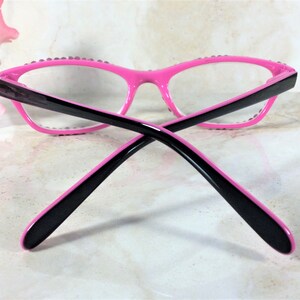 Pu&ograve; includere: Occhiali rosa acceso con aste nere e lenti trasparenti. Le montature sono decorate con piccoli abbellimenti scintillanti. Gli occhiali hanno un design moderno a occhi di gatto.