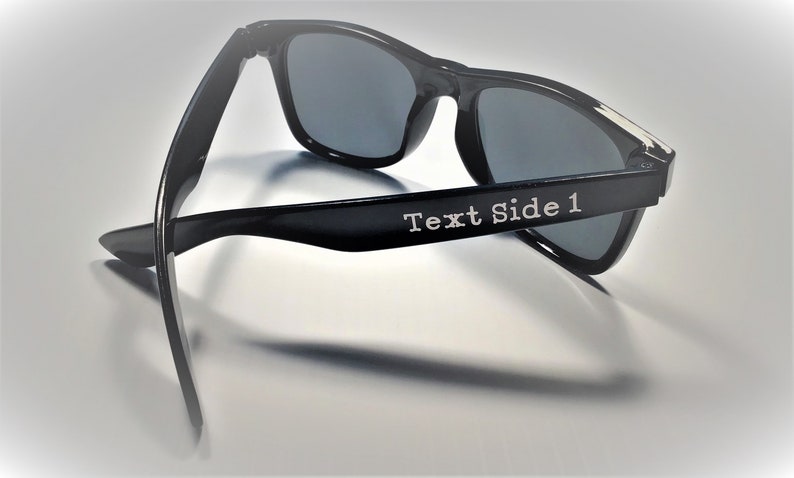 May include: Black sunglasses with a dark gray lens. The sunglasses have the text "Text Side 1" on the side.