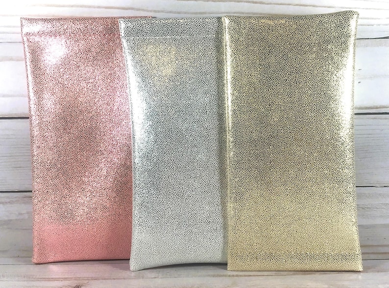 Puede incluir: Tres estuches rectangulares para gafas en fila. Los estuches son rosas, plateados y dorados, cada uno con un acabado texturizado y moteado. Los estuches est&aacute;n hechos de un material brillante y est&aacute;n de pie.