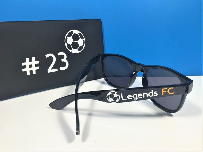May include: Black sunglasses with a white soccer ball and the text "Legends FC" on the side. The sunglasses are in a black case with a white soccer ball and the number "#23" on the front.