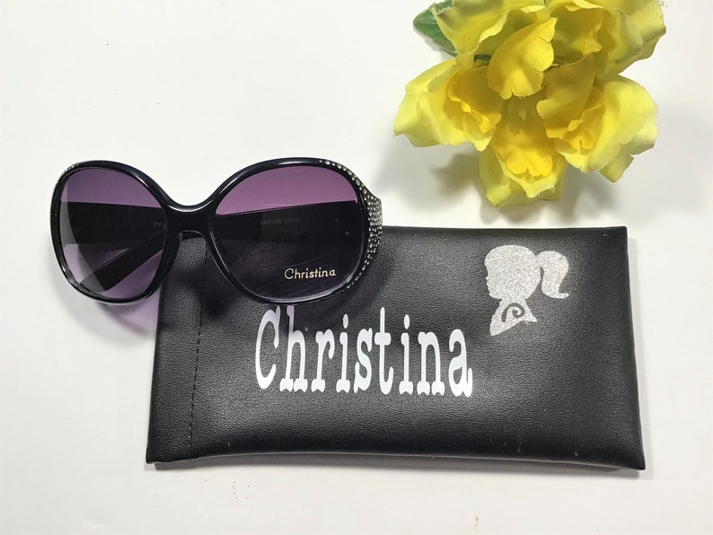 May include: Black sunglasses with a rhinestone trim and a black leather case with the name "Christina" printed on it in white.