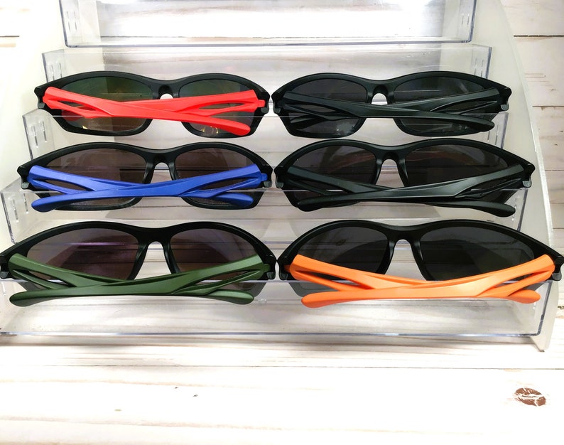 May include: Six pairs of black sunglasses with different colored frames. The frames are red, blue, green, and orange.