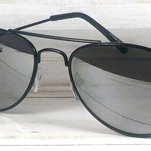 May include: Aviator sunglasses featuring a thin black metal frame and a double bridge design. The lenses are reflective and silver in color, providing a mirrored finish. The temples are black with curved ends, and the nose pads are clear and adjustable.