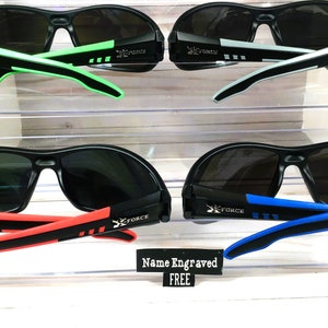 May include: Four pairs of black sunglasses with different colored accents on the arms. The sunglasses have a dark gray lens. The text "X FORCE" is printed on the arms of the sunglasses. The text "Name Engraved FREE" is printed on a white tag.