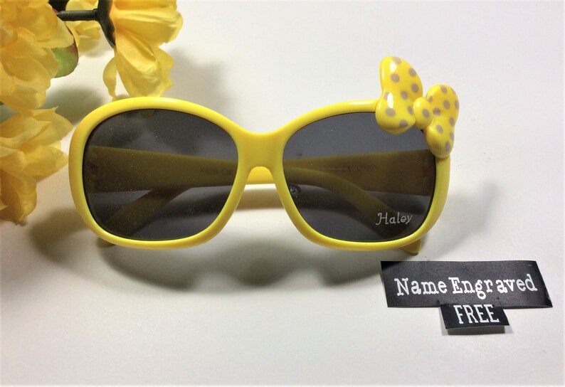 Puede incluir: Gafas de sol amarillas con un lazo de lunares en el lateral. Las gafas tienen lentes negras y el nombre "Haley" est&aacute; grabado en la lente derecha. El texto "Nombre grabado GRATIS" est&aacute; en una etiqueta negra.