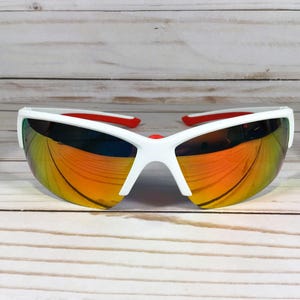 May include: Sport sunglasses featuring a white frame and a single continuous wrap-around lens with a reflective orange and yellow gradient finish. The interior of the frame arms and the nose bridge pads are accented with a bright red colour.