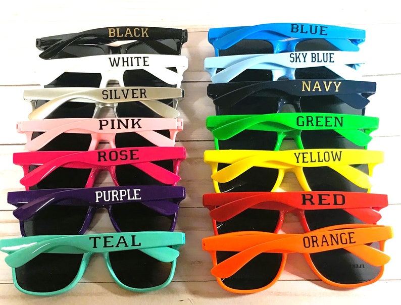 May include: A set of 14 colorful plastic sunglasses with different colored frames and lenses. Each pair has a different color name printed on the frame, including black, white, silver, pink, rose, purple, teal, blue, sky blue, navy, green, yellow, red, and orange.