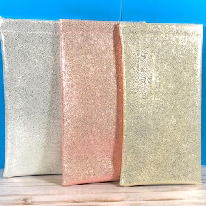 Peut inclure: Trois pochettes rectangulaires avec une finition textur&eacute;e et scintillante. La pochette de gauche est argent&eacute;e, celle du milieu est or rose et celle de droite est dor&eacute;e. Chaque pochette a un bord sup&eacute;rieur plat et une orientation verticale.