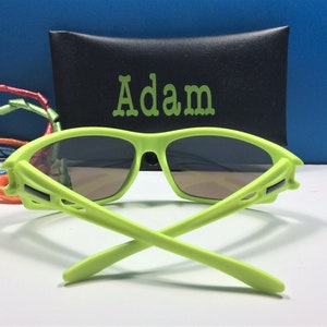 Puede incluir: Gafas de sol de color verde lima con una funda negra que dice "Adam".
