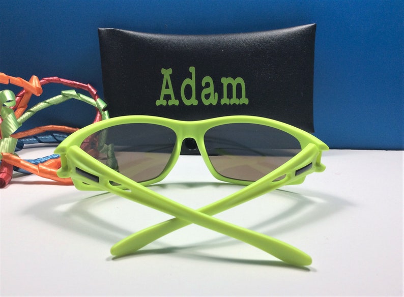 Puede incluir: Gafas de sol de color verde lima con una funda negra que dice "Adam".