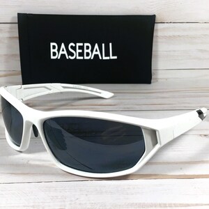 May include: White sports sunglasses with dark lenses are displayed in front of a black case. The case has the word "BASEBALL" printed in white. The sunglasses have a sporty design.