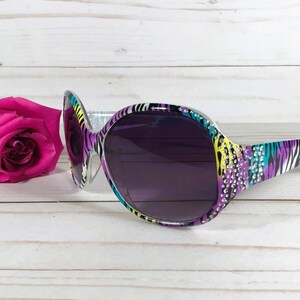 May include: Purple, yellow, and blue zebra print sunglasses with rhinestones on the frame. The sunglasses have dark lenses.