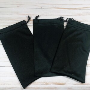 May include: Three rectangular black drawstring pouches made of a soft, smooth fabric. Each pouch features a black cord threaded through the top hem, allowing the bag to be cinched closed. The pouches are arranged side by side in a row.