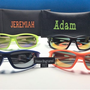 Puede incluir: Cuatro pares de gafas de sol con diferentes colores de montura y lentes. Las gafas de sol est&aacute;n dispuestas en dos filas de dos. La fila superior presenta un par de gafas de sol verdes con una funda negra etiquetada como "JEREMIAH" y un par de gafas de sol negras con una funda negra etiquetada como "Adam". La fila inferior presenta un par de gafas de sol azules y un par de gafas de sol naranjas. Un cartel en el medio de la imagen dice "Nombre grabado GRATIS".