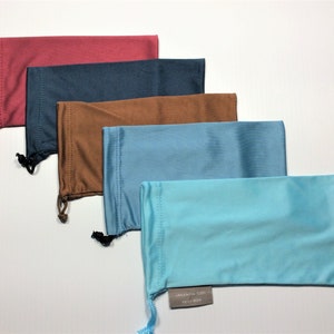 May include: Five different colored drawstring pouches for glasses. The pouches are lined up from top to bottom in the following order: red, dark blue, brown, light blue, and turquoise.