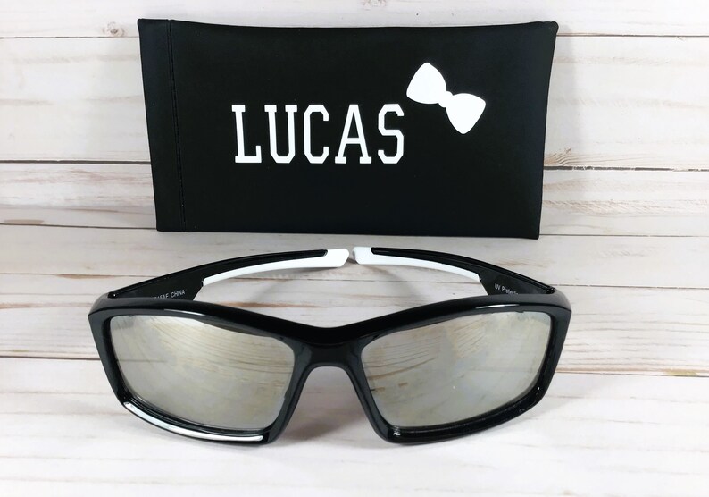 May include: Black sunglasses with mirrored lenses and white accents. The sunglasses come with a black carrying case that has the name "LUCAS" and a white bow tie printed on it.