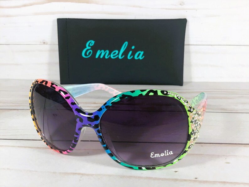 May include: Rainbow leopard print sunglasses with rhinestones and a black case with the word "Emelia" printed on it.