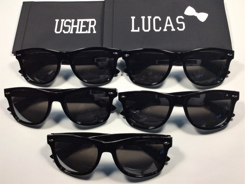 May include: Four pairs of black sunglasses with dark lenses. The sunglasses are arranged in two rows of two. The top row has the words "USHER" and "LUCAS" on the boxes behind them.