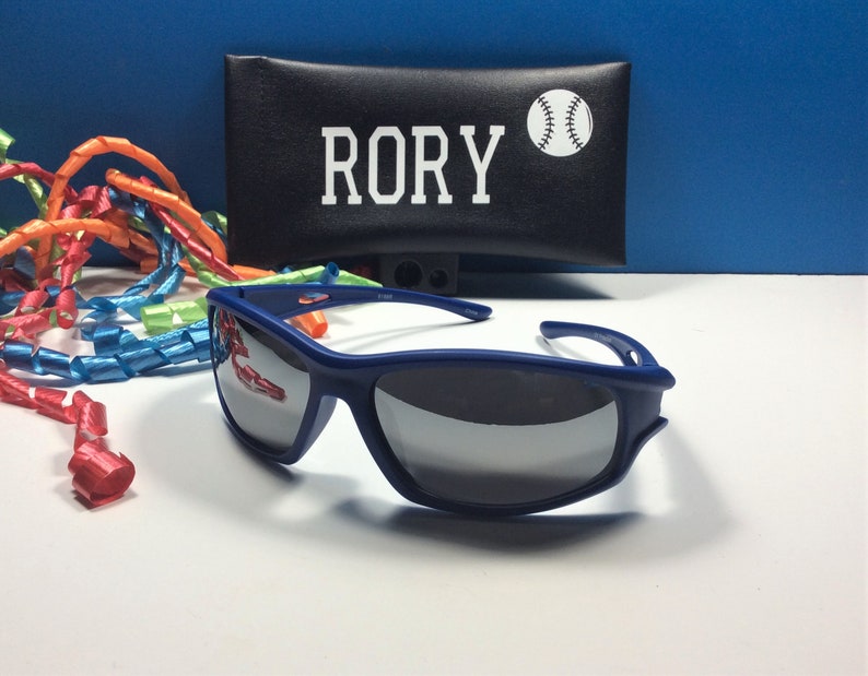 Puede incluir: Gafas de sol azules con lentes espejados y una funda negra con el nombre "RORY" y un gr&aacute;fico de b&eacute;isbol blanco.