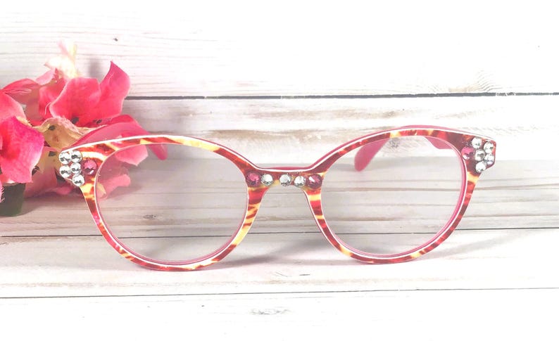 May include: Eyeglasses with a red and yellow tortoiseshell pattern frame, featuring clear lenses and decorative rhinestones embedded along the bridge and outer corners of the frame front, providing a detailed and ornate appearance.