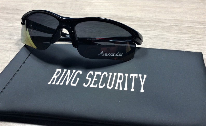 May include: Black sunglasses with a gold tint on the lenses and a black case with the text "RING SECURITY" printed in white.