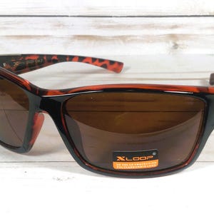 May include: Brown-tinted sunglasses with a black frame and red-brown patterned accents. The sunglasses have a rectangular shape and a curved design. The lenses are brown and the frame has a glossy finish. The brand name "XLOOP" is visible on a sticker.