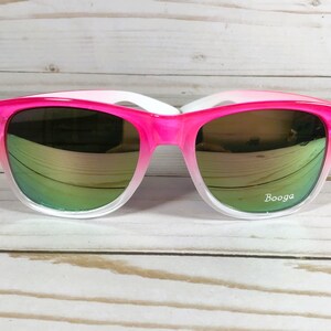 Puede incluir: Gafas de sol con degradado rosa y blanco con lentes espejados verdes. Las gafas tienen la palabra "Booga" impresa en la lente derecha.