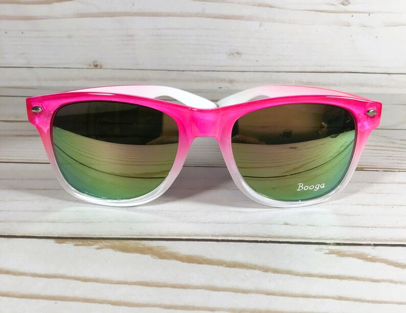 Puede incluir: Gafas de sol con degradado rosa y blanco con lentes espejados verdes. Las gafas tienen la palabra "Booga" impresa en la lente derecha.