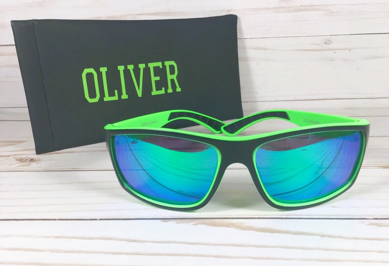 K&ouml;nnte beinhalten: Schwarze Sonnenbrille mit gr&uuml;nen Rahmen und verspiegelten Gl&auml;sern. Die Sonnenbrille befindet sich in einem schwarzen Etui mit dem Namen "OLIVER" in gr&uuml;ner Schrift.