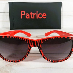 May include: Red and black zebra print sunglasses with dark gray lenses. The sunglasses are in a black case with the word "Patrice" printed in red.