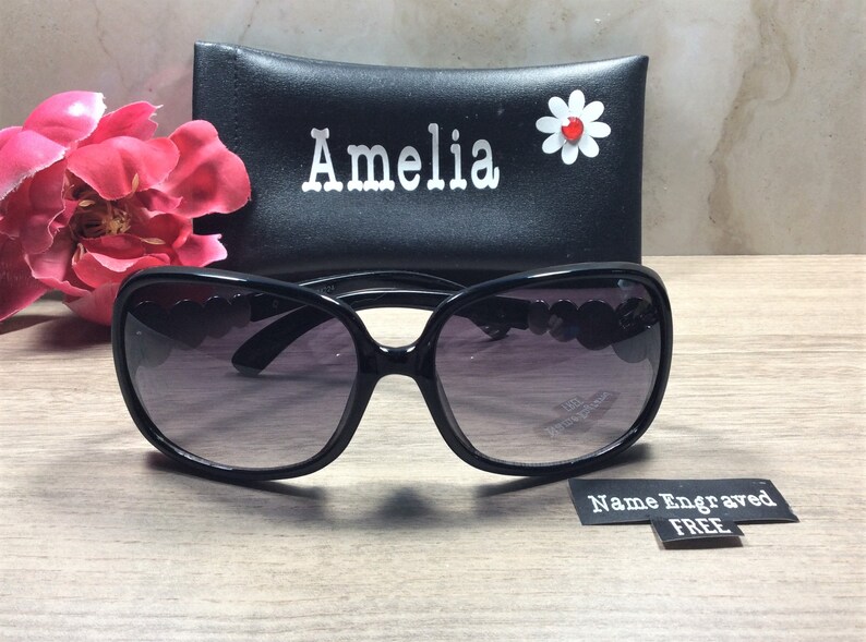 Puede incluir: Gafas de sol negras con un dise&ntilde;o en forma de coraz&oacute;n en las patillas. Las gafas de sol vienen con una funda negra con el nombre "Amelia" grabado y una margarita blanca con un centro rojo.
