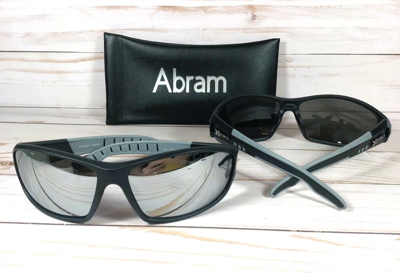 May include: A pair of black sunglasses with mirrored lenses and gray accents. The sunglasses are in a black case with the name "Abram" printed on it.