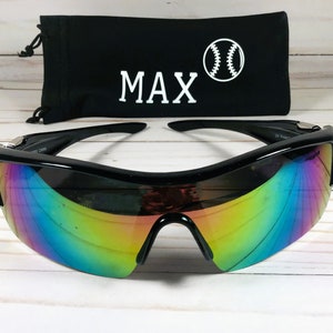 May include: Black sunglasses with rainbow mirrored lenses and a black carrying case with the name "MAX" and a baseball graphic.