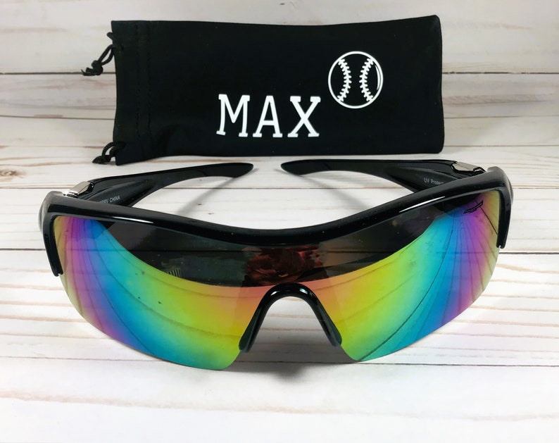 May include: Black sunglasses with rainbow mirrored lenses and a black carrying case with the name "MAX" and a baseball graphic.