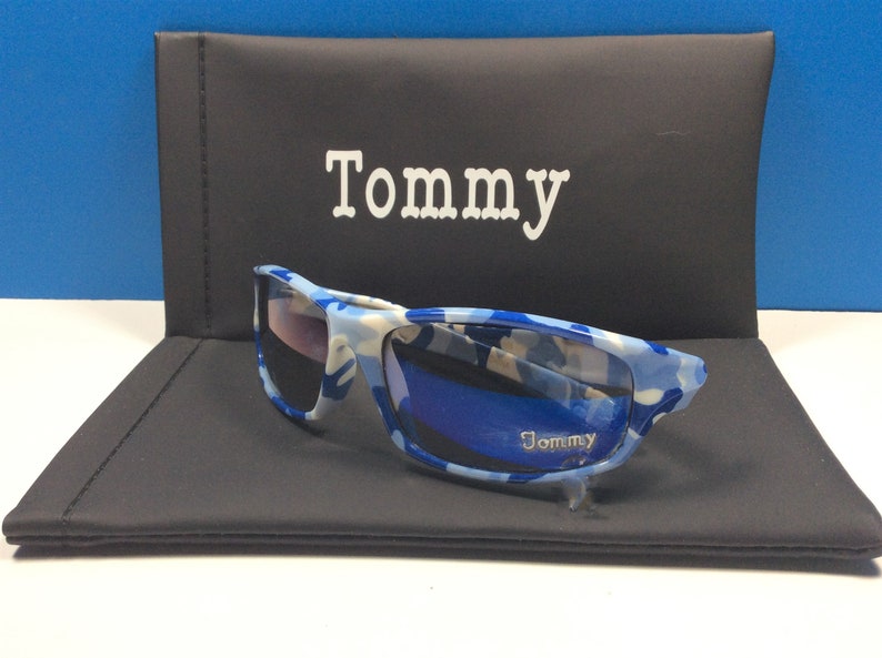 May include: Blue and white camouflage sunglasses with a black case. The case has the word "Tommy" printed on it.