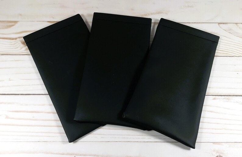 May include: Three black fabric placemats, folded and stacked on a white wooden surface.